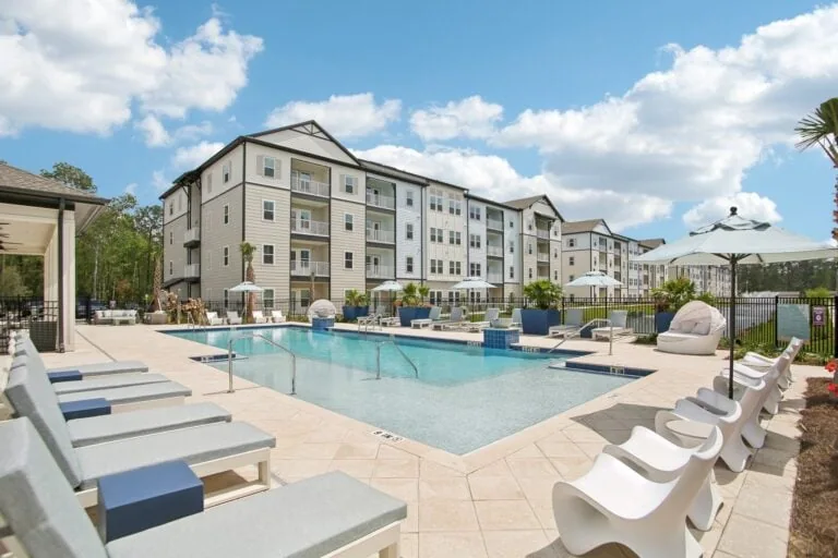 image of apartment building overlooking a pool with lounge chairs on a sunny day