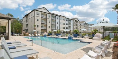 image of apartment building overlooking a pool with lounge chairs on a sunny day